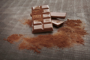 Broken chocolate pieces and cocoa powder on wooden background