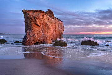 El Matador Beach rock bathed in reddish sunlight at sunset