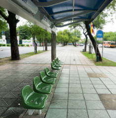 empty green chair at the public bus stop on the footpath.