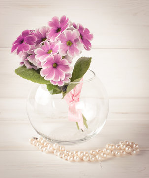 Bouquet of primroses in round vase and women's pearl necklace