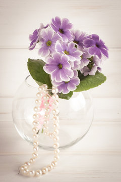 Bouquet of primroses in round vase and women's pearl necklace
