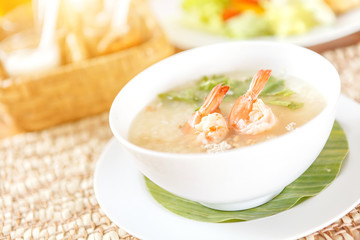 Traditional Thai porridge rice gruel and shrimp in white bowl with seasoning background on wood table in sunlight.