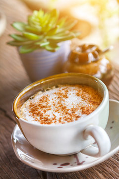 Cup of hot coffee on wood table with succulent and sunlight background.