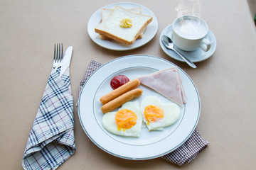 Breakfast with fried egg, ham, sausage, toast, butter, and coffee on table.