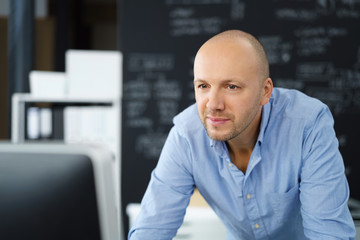 lächelnder mann im büro schaut auf seinen computer