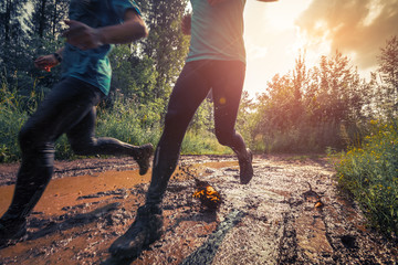 Two trail running athletes crossing the dirty puddle