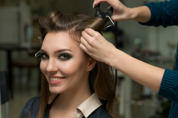Naklejka premium Hair stylist making ringlets to brunette woman. Hairdresser work