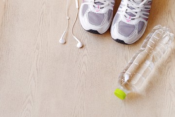 fitness concept with Exercise Equipment on wooden background.White phone with headphones and running shoes on wooden background and copy space.