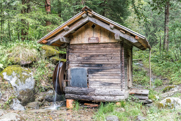 Minimühle mit Wasserrad in einem Waldstück in den Alpen
