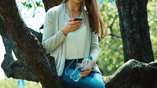 Teenage girl using cell phone outdoors sitting on tree
