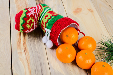 On the table is a colorful Christmas sock. Nearby are tangerine and spruce branches.
