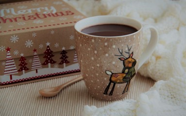 Cup of cocoa in woolen scarf. Christmas background.