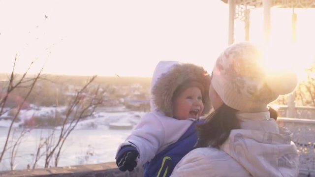 Beautiful happy young Family having fun outdoors at winter. Happy laughing mother with little baby boy playing in winter park with sun and sunshine. Mom and with a child with snow. Slow motion, Slowmo