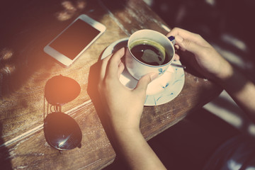 Close-up Of Woman Holding Mobile Phone In Front Of Coffee Cup