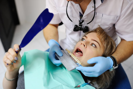 Male dentist examines the mouth and teeth of a patient woman. Selecting the color of teeth
