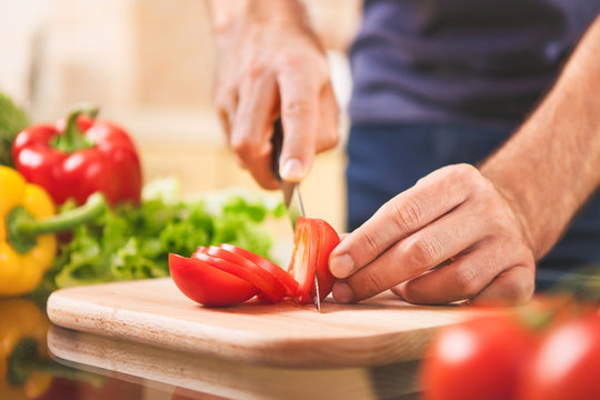 close up of male hand cutting tomato on cutting board