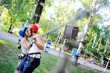 Asian girl and a guy are obstacles on the road rope. Extreme vacation. Man and woman in a special helmet and a safety ekiperovke kissing on park background