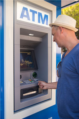 Man using ATM to withdraw cash. Smiling young businessman standing in front of an ATM and looking....