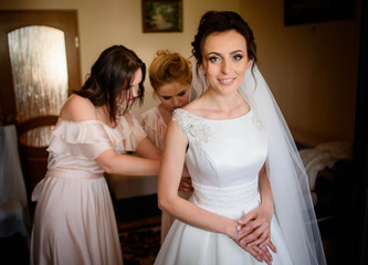 beautiful bridesmaids helping the happy bride getting dressed