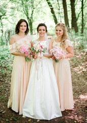 happy and young bride and her bridesmaids standing together