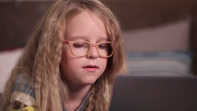 Beautiful little girl using computer in bedroom