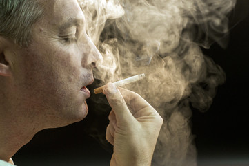 Fototapeta premium Man smoking against a black background, Cigarette addiction. 