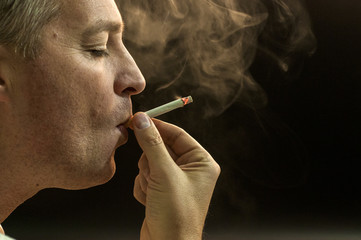 Fototapeta premium Man smoking against a black background, Cigarette addiction. 