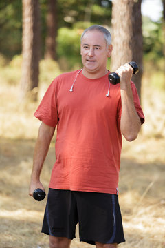 smiling male athlete exercising with weight in a park