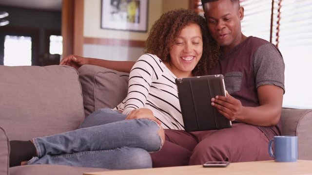 Millennial couple sitting on couch watching movie on their tablet computer