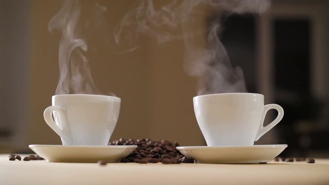 Two white cups of delicious coffee on the table with roasted beans in 4K