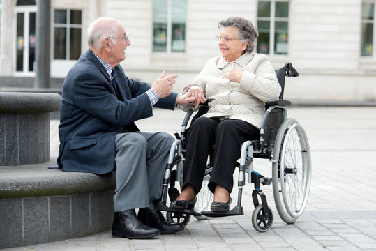 old couple a man and woman sitting in wheelchair outdoors