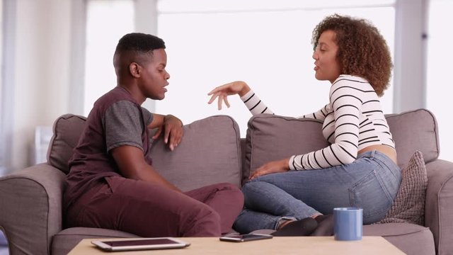 African American man and woman talk while relaxing on their couch in their living room