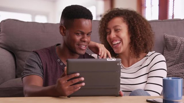Authentic millennial black couple sits on floor watching a video on their tablet