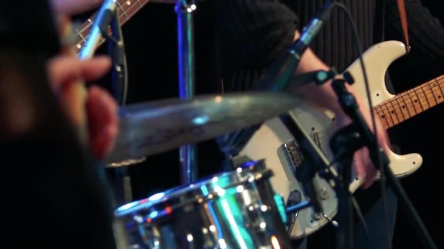 Men stand on stage and play on drums and guitar - close-up of hands