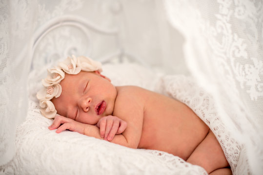 Ideas for newborn photo shoot. Newborn girl sleeping on the tummy to decorative crib. Portrait of a sleeping newborn girl with floral bandage on his head covered with delicate tippet