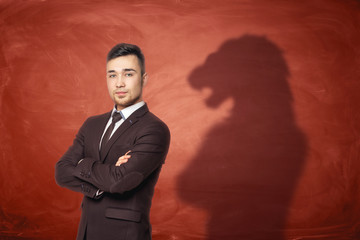 Businessman standing with hands across and his shadow on red empty blackboard behind looking like...