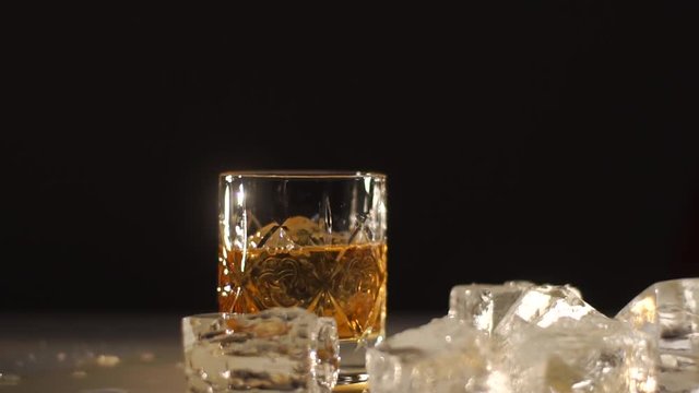 an ice ball falling down into glass with wiskey. Drink is spleshing on the sides. Dark and shadows