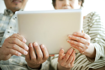 タブレットPCを持つシニア夫婦の手元 © ohayou!