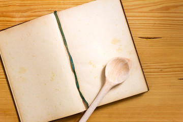 Geöffnetes vergilbtes Kochbuch mit leeren Seiten und Kochlöffel auf Holz Hintergrund