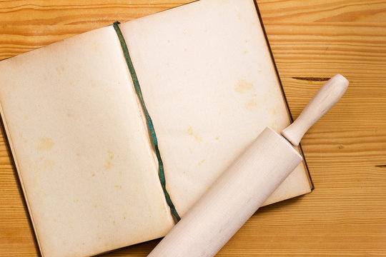 Ge&ouml;ffnetes vergilbtes Backbuch mit leeren Seiten und Nudelholz auf Holz Hintergrund