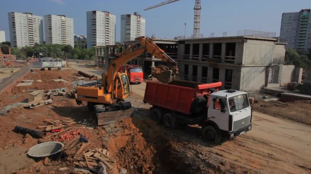 Industrial machines, excavator loads truck at construction site, aerial shot