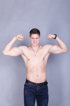 young man with relief muscles in jeans with a naked torso on a gray background