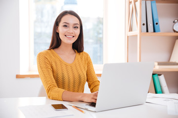 Cheerful businesswoman using laptop and looking at camera