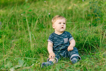 chubby little boy in dark clothes sitting on the grass in the park on a summer day