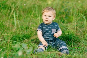 chubby little boy in dark clothes sitting on the grass in the park on a summer day