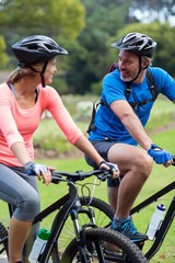 Naklejka premium Athletic couple looking face to face while riding bicycle