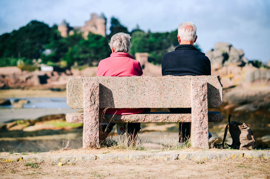 Zwei alte Menschen auf einer Bank/Frau und Mann sitzen auf einer Steinbank und schauen in die Ferne