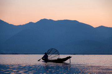 Naklejka premium Intha fisherman fishing at sunset in his typical canoe with fish
