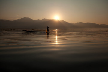 Intha fisherman fishing at sunset in his typical canoe with fish
