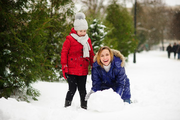 Mother with daughter build a snowman in park.